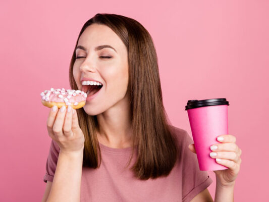 Girl attempting to eat a donut with cup in another hand